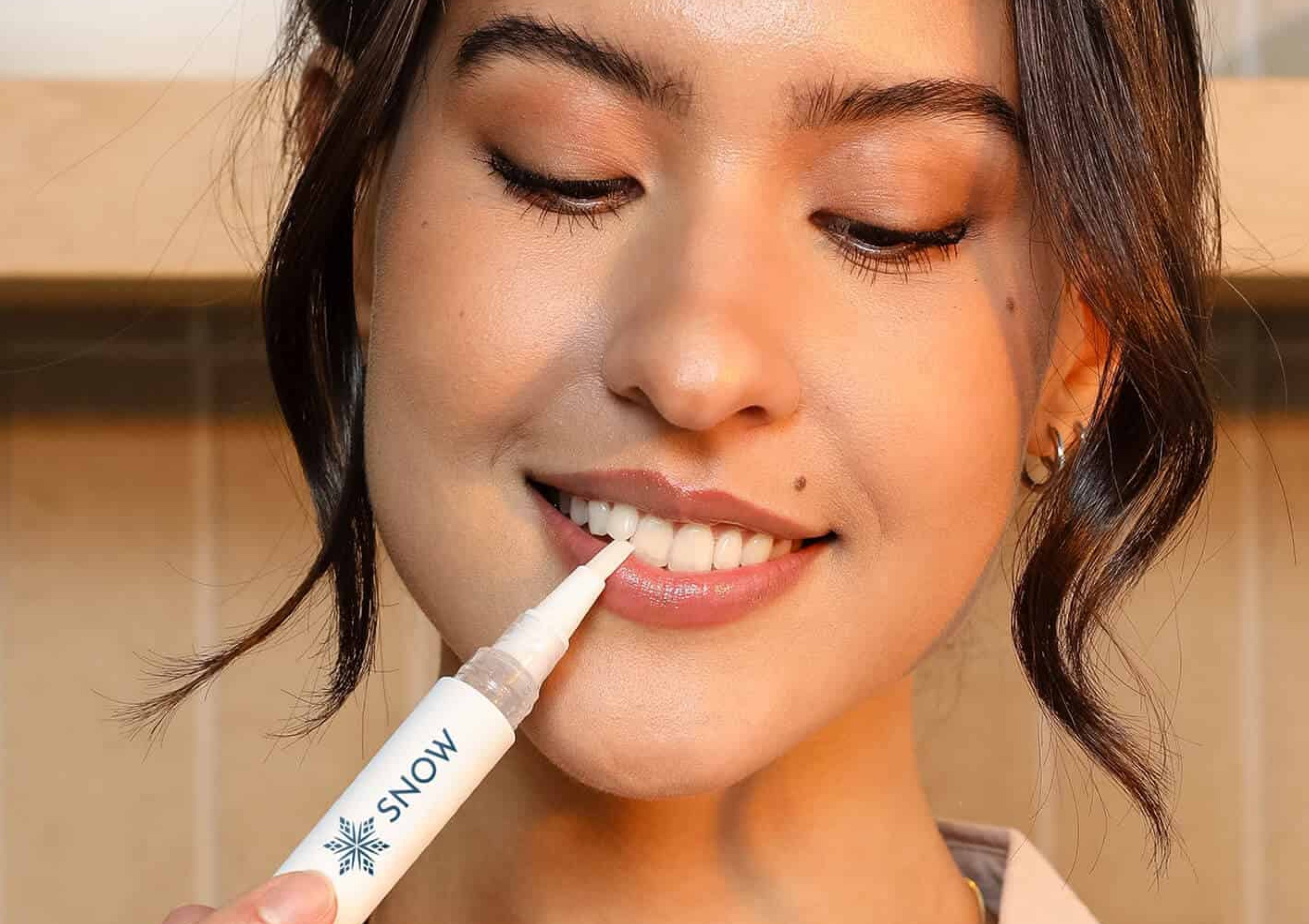 A person using a Snow teeth whitening pen on their teeth.